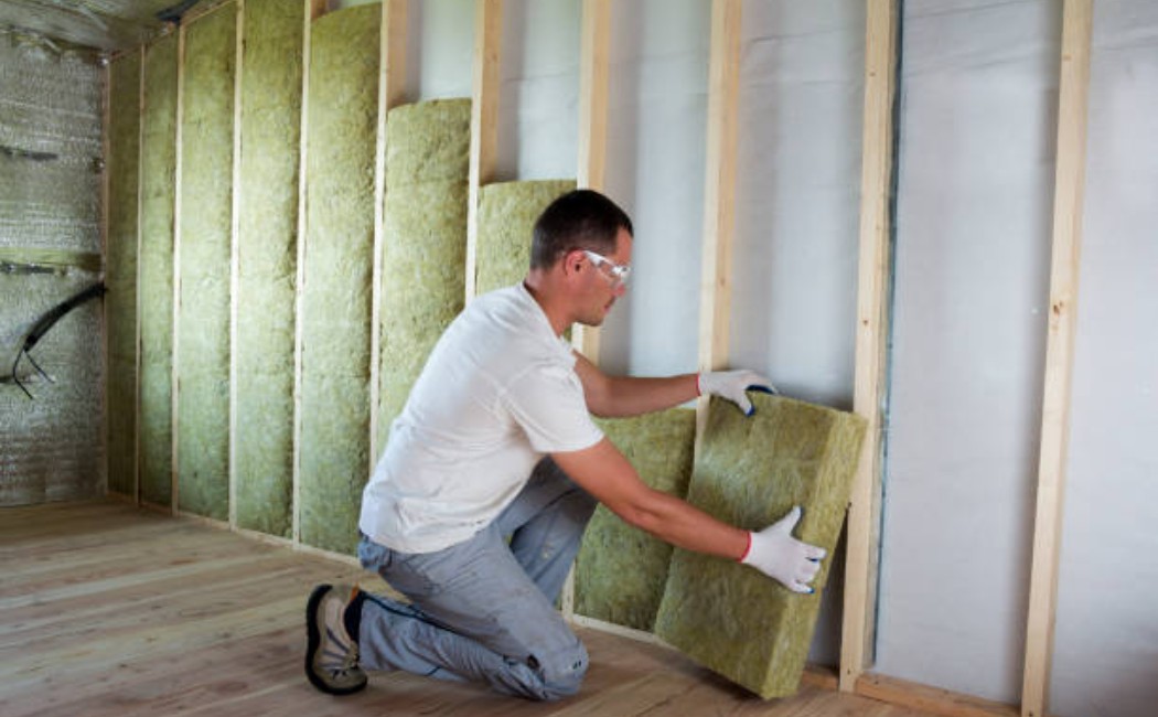 A Professional wearing a respirator and safety gear is installing thermal insulation in a home.