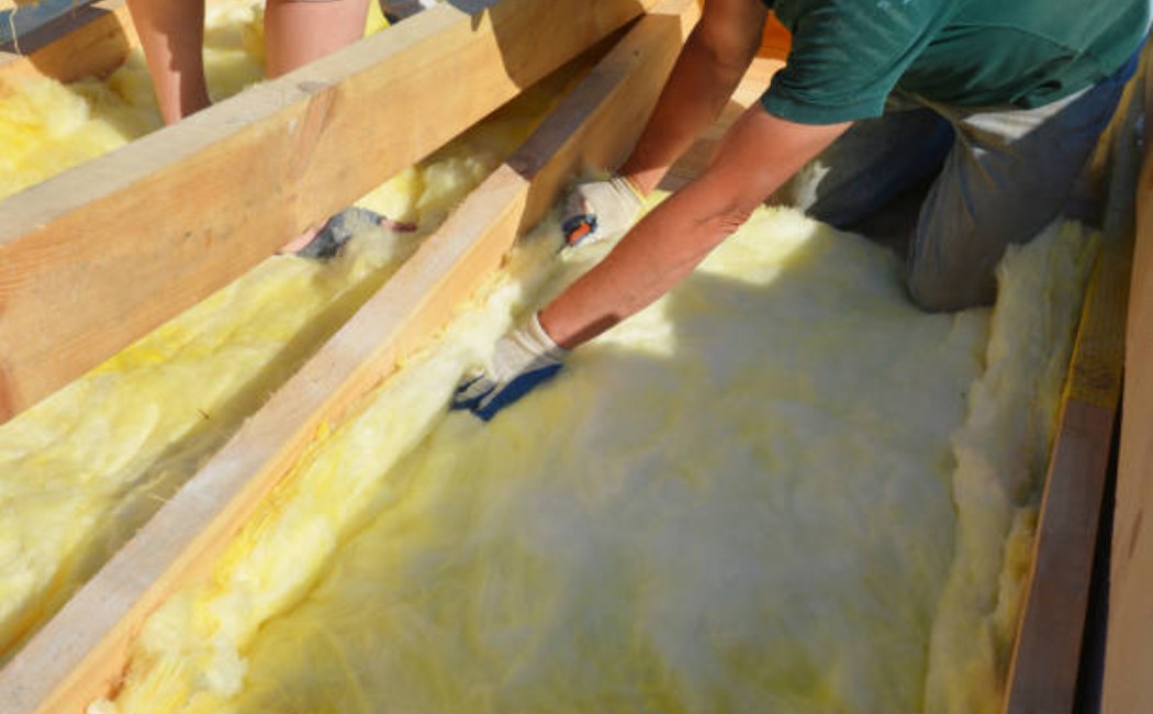 Contractors installing glass-wool insulation batts on a wall interior