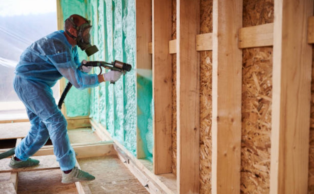 Construction worker spraying polyurethane foam insulation into a wooden frame wall.