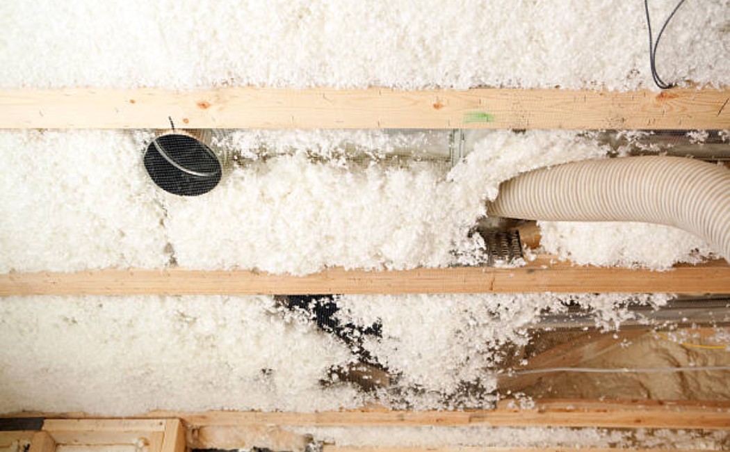 Worker installing blown insulation between wooden floor joists