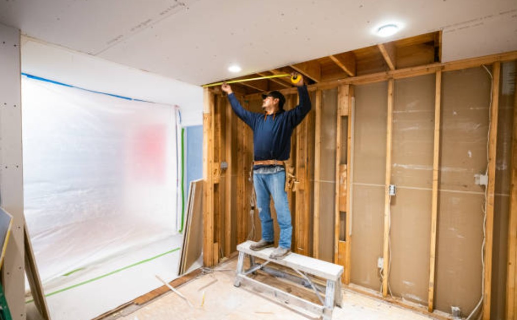 Two construction workers are installing drywall sheets on the kitchen walls