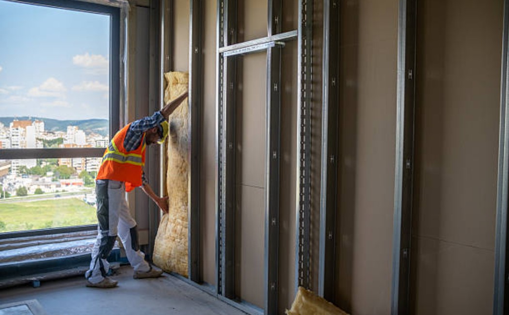 Drywall worker installing mineral wool insulation on a construction site wall