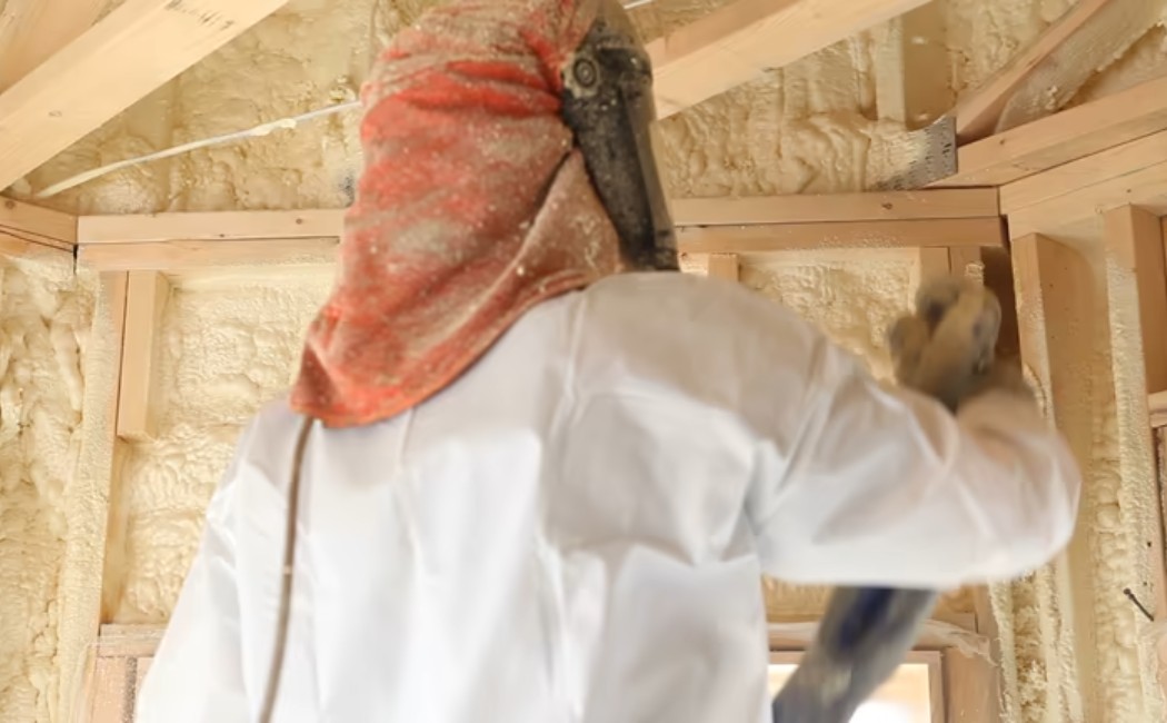 Builder using a foam gun to spray polyurethane insulation into wall cavities.