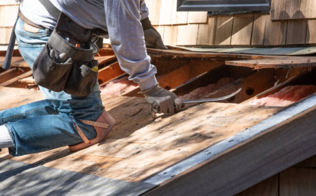 Roofer removing old shingles from a house roof during renovation.