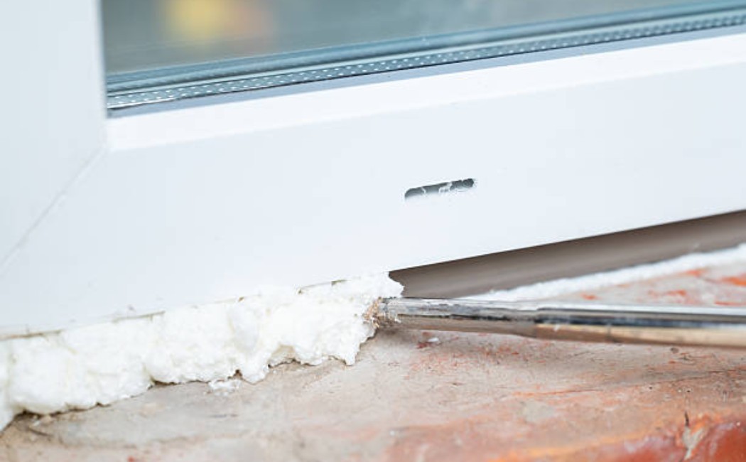 Worker filling gaps with spray foam during window installation