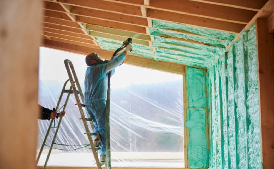 Worker spraying foam insulation on wooden house frame