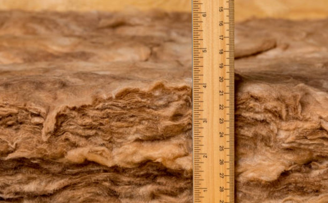 Checking fiberglass insulation thickness in the ceiling cavity with a ruler.