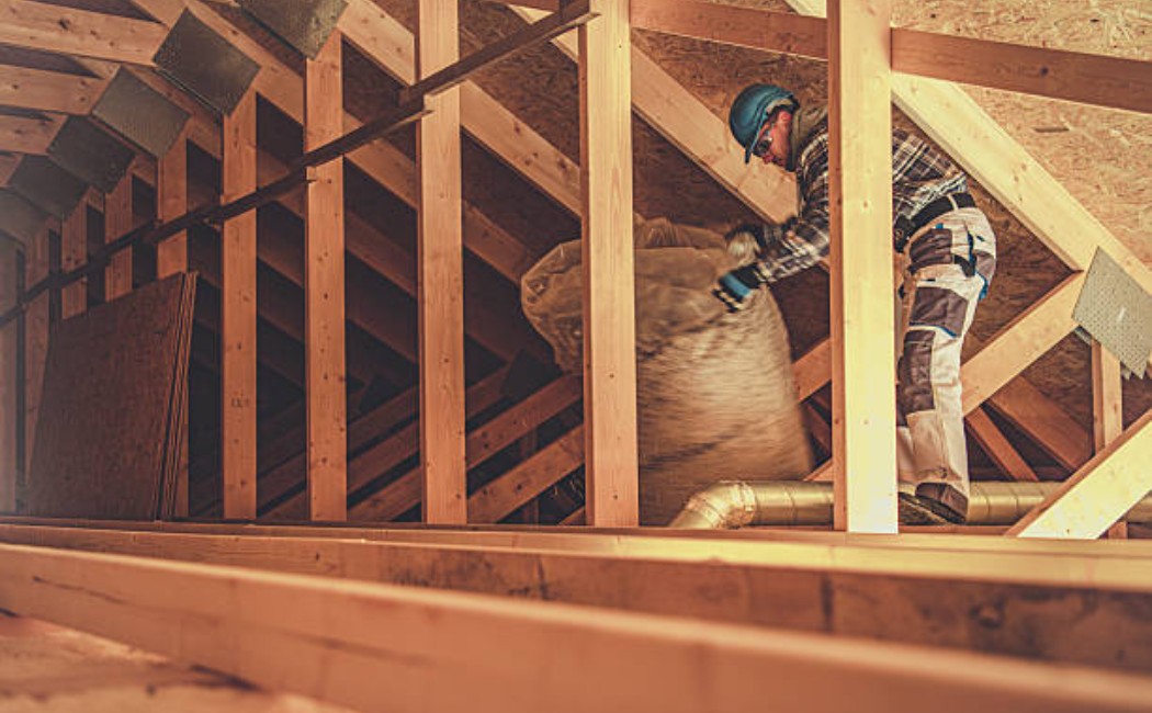 Worker installing attic insulation during home renovation.