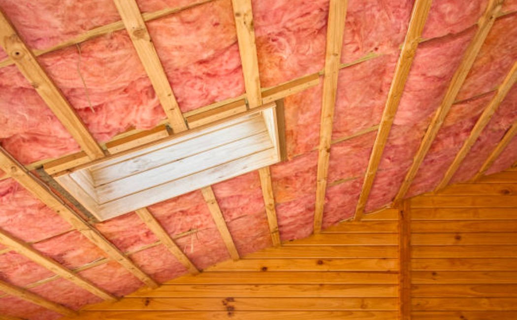 Insulation is being installed between rafters in a sloped attic ceiling.