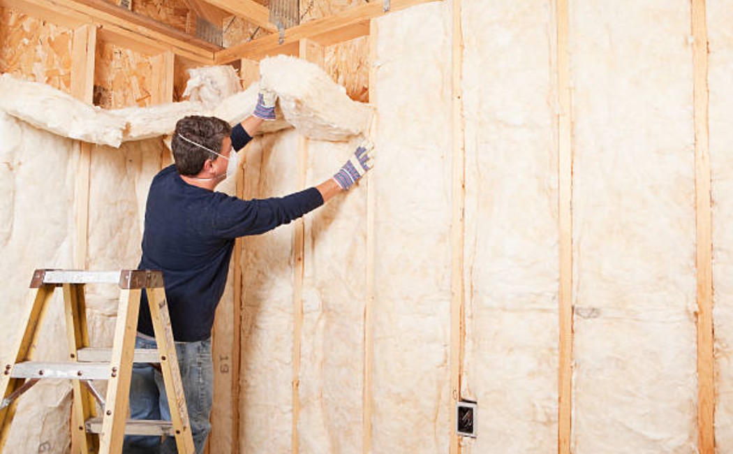 Worker placing fiberglass batt insulation in the wall frame.